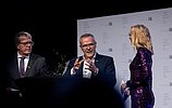 Drei Personen stehen bei einer Veranstaltung der Handwerkskammer Köln auf der Bühne. Zwei Männer im Anzug und eine Frau im glitzernden violetten Kleid unterhalten sich vor einer Bühne mit dem Logo der Handwerkskammer Köln.