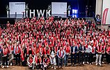 Große Gruppe von Menschen bei einer Meisterfeier der Handwerkskammer Köln im RHEIN SIEG FORUM. Viele Teilnehmende tragen rote Schals mit der Aufschrift „Handwerksmeister“ und stehen gemeinsam für ein Gruppenfoto vor der Bühne.
